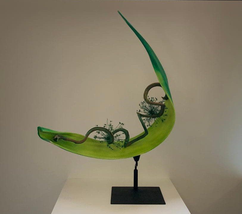 A green sculpture of two bicycles on top of a black stand.
