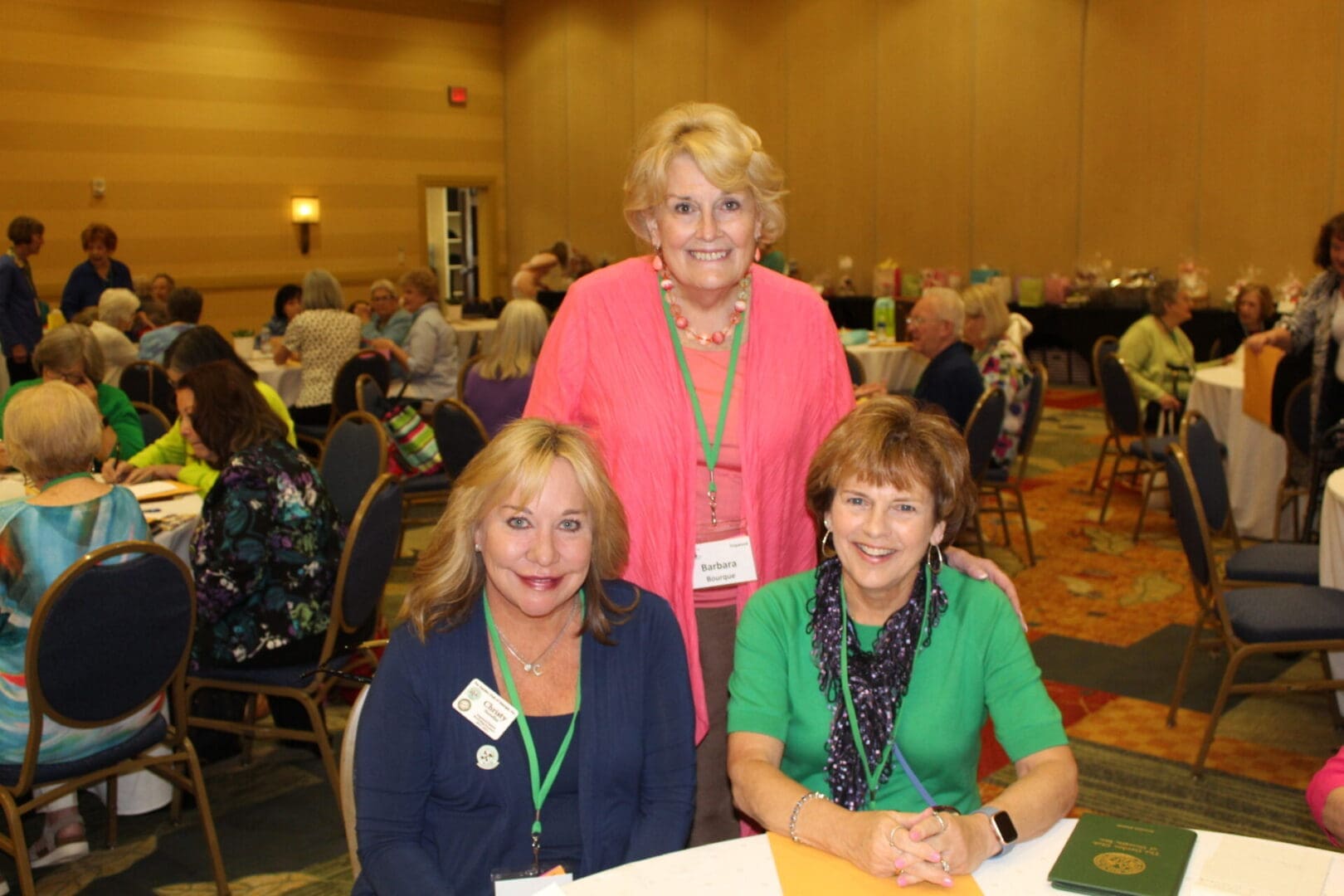 Three women sitting at a table in front of a crowd.
