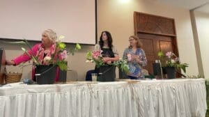 Three women sitting at a table with flowers.