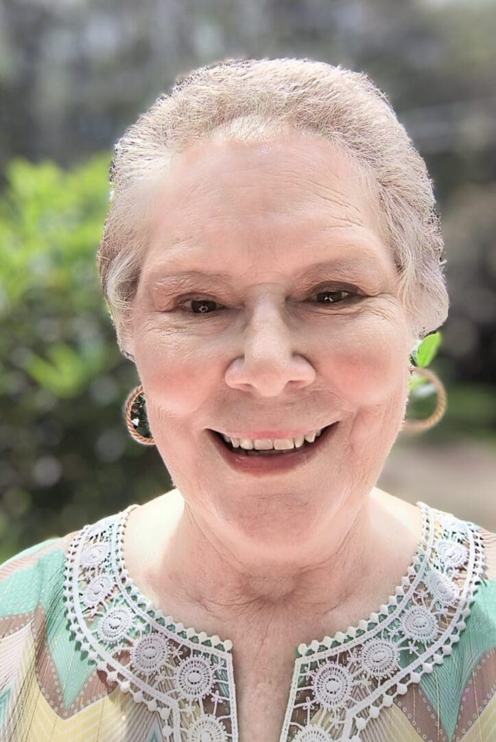 A smiling elderly woman wearing hoop earrings and a light-colored top.