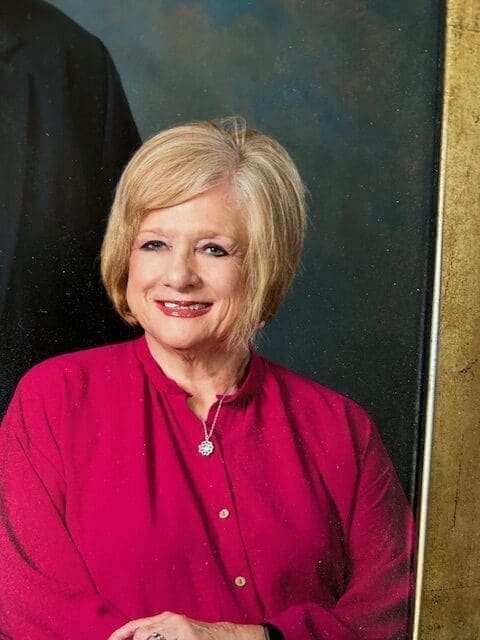 A smiling woman in a red blouse with blonde hair.