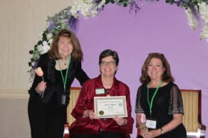 Three women smiling with an award certificate.