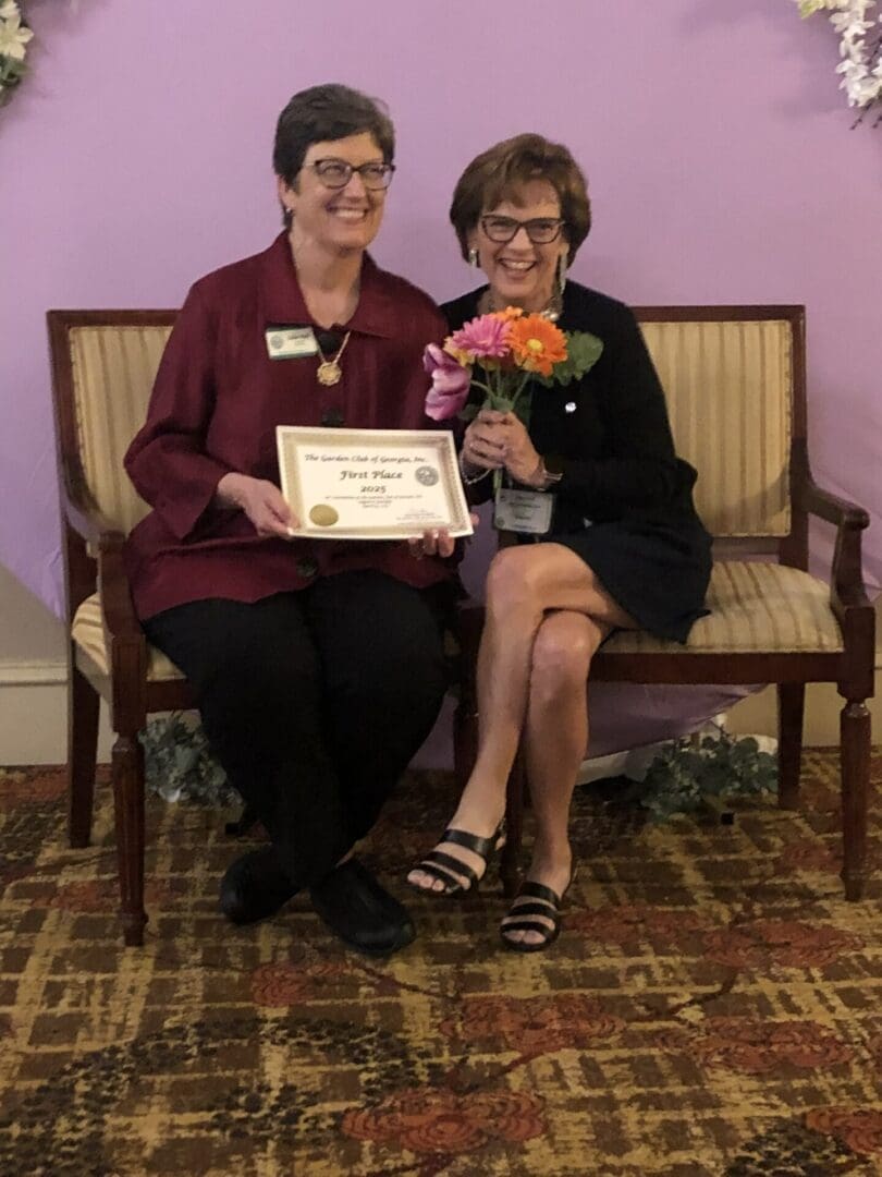 Two women sitting with certificate and flowers.